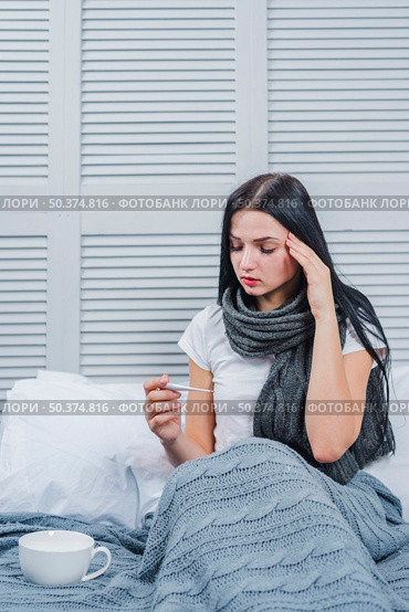 sick young woman sitting bed looking thermometer. Стоковое фото, агентство Ingram Publishing / Фотобанк Лори