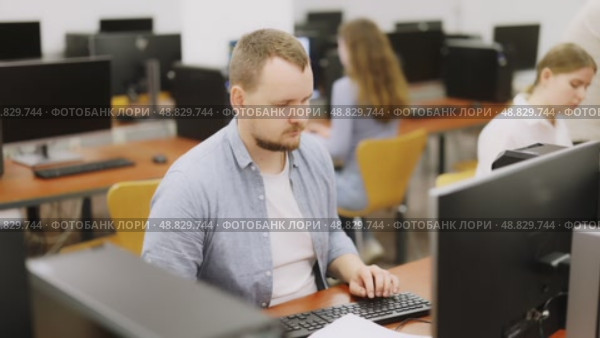 Side view on concentrated male student sitting at library desk with pc, preparing for exam in computer class. Стоковое видео, видеограф Яков Филимонов / Фотобанк Лори