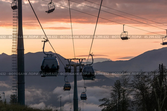 Ski gondolas glide above misty mountains at sunset, offering stunning views of the vibrant sky and surrounding landscape. Стоковое фото, фотограф Алексей Климкин / Фотобанк Лори