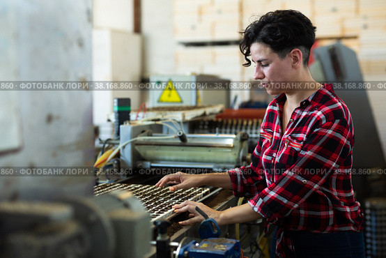 Skilled farmer woman working with automatic filling and seeding line for growing containerized seedlings of decorative plants in greenhouse. Стоковое фото, фотограф Яков Филимонов / Фотобанк Лори