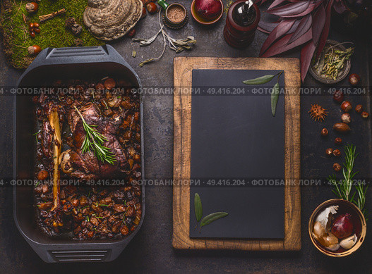 Slow cooked venison roast in black cast iron pan, top view. Braised leg of deer with bone and roasted vegetables in pot on dark rustic kitchen table background with copy space for design, top view. Стоковое фото, агентство Ingram Publishing / Фотобанк Лори