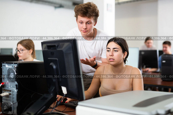 Smart teen schoolboy helping cute girl classmate sitting at computer during informatics lesson. Стоковое фото, фотограф Яков Филимонов / Фотобанк Лори