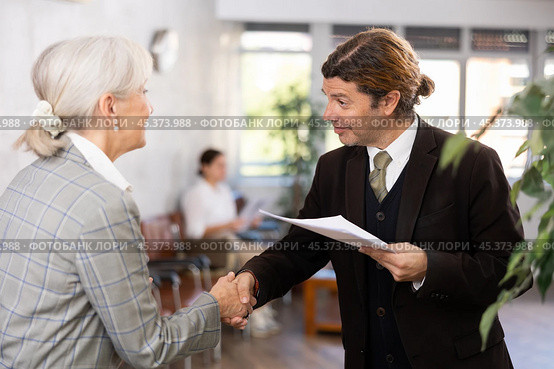 Smiling businessman with papers shaking hands with elderly woman. Стоковое фото, фотограф Яков Филимонов / Фотобанк Лори