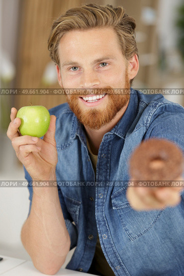 smiling man holding a donut and an apple. Стоковое фото, агентство Ingram Publishing / Фотобанк Лори