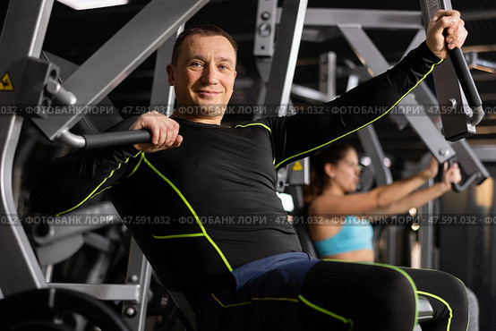 Smiling man performing chest press in exercise machine. Стоковое фото, фотограф Яков Филимонов / Фотобанк Лори