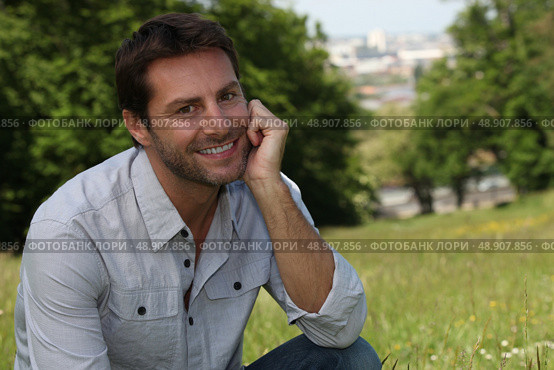 Smiling man sitting in a park. Стоковое фото, агентство Ingram Publishing / Фотобанк Лори