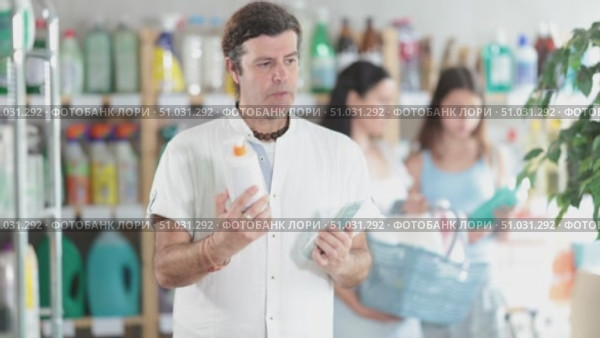Smiling man with long curly hair comparing sunscreen and tanning lotion, picking best option for summer family vacation in personal care store while wife and daughter browsing products in background. Стоковое видео, видеограф Яков Филимонов / Фотобанк Лори