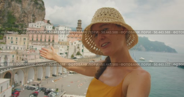 Smiling woman gestures toward colorful cliffside buildings in Amalfi Italy during summer trip. Стоковое видео, видеограф Igor Tichonow / Фотобанк Лори