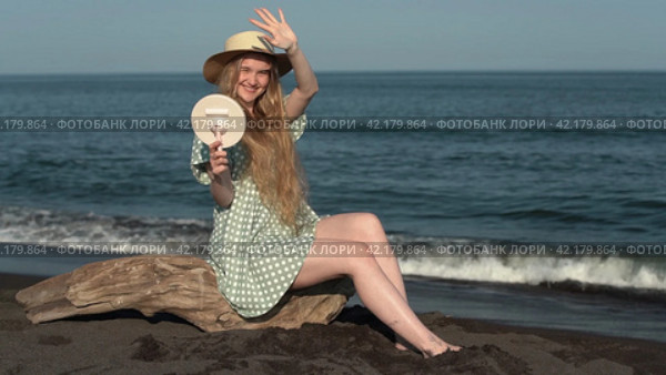Smiling young woman holds mirror in her hand and closes herself with other hand from sun's rays. Стоковое видео, видеограф А. А. Пирагис / Фотобанк Лори