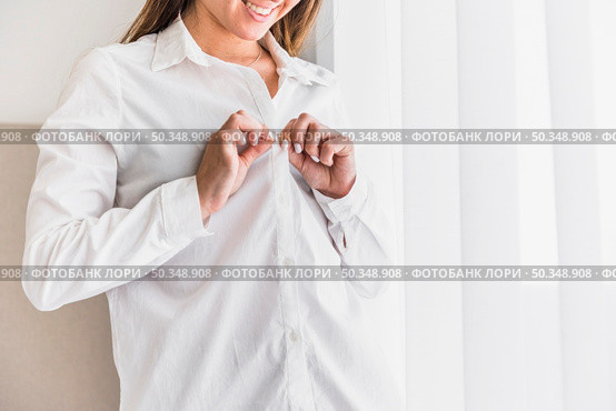 smiling young woman putting button her white shirt. Стоковое фото, агентство Ingram Publishing / Фотобанк Лори