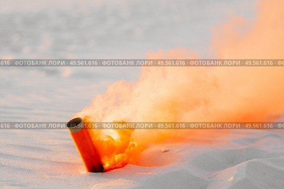 smoke bomb with orange smoke stuck in the white sand. Стоковое фото, агентство Ingram Publishing / Фотобанк Лори