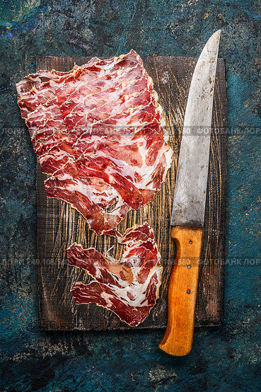Smoked pork meat from coppa with kitchen knife on rustic wooden background. Traditional Italian specialty made from pork neck . Top view. Стоковое фото, агентство Ingram Publishing / Фотобанк Лори