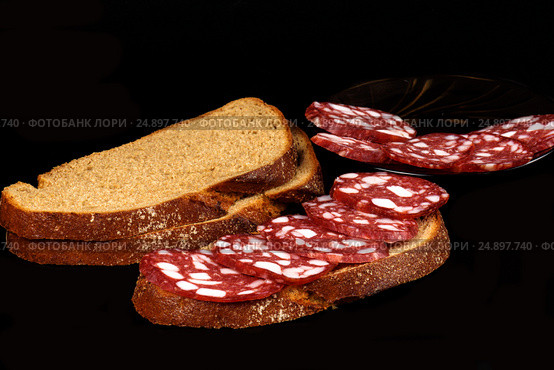Smoked sausage and bread on a black background. Стоковое фото, фотограф Artem Sobov / Фотобанк Лори