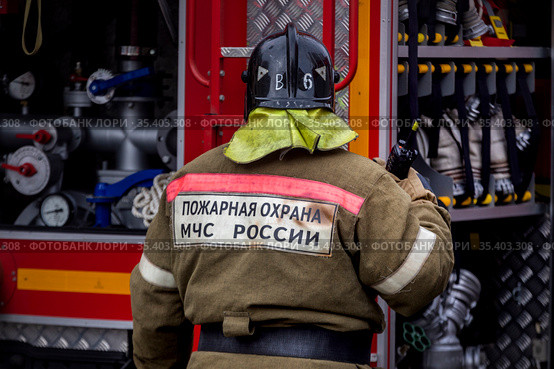 Сотрудник пожарного расчета стоит у пожарной машины во время тушения пожара в центре города Москвы, Россия (2021 год). Редакционное фото, фотограф Николай Винокуров / Фотобанк Лори
