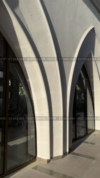 Современное здание с арочными элементами на фоне голубого неба The villa is a modern, white Mediterranean-style house with arched doorways, large balconies, and light stone elements, surrounded by a landscaped rocky garden and a clear blue sky. Стоковое видео, видеограф Zita Khasanova / Фотобанк Лори