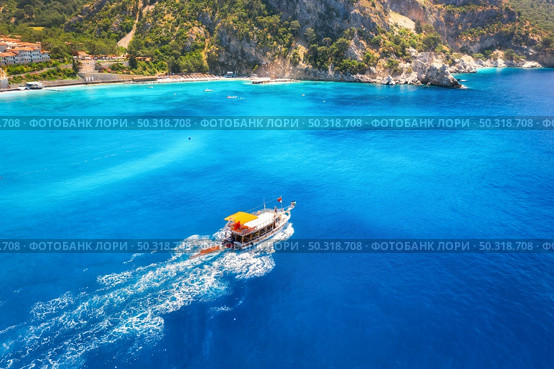 Speed boat in blue sea at sunrise in summer. Aerial view of floating motorboat in sea bay. Tropical landscape with yacht, clear water, rocks , stones, mountain, green trees. Top view. Oludeniz, Turkey. Стоковое фото, агентство Ingram Publishing / Фотобанк Лори