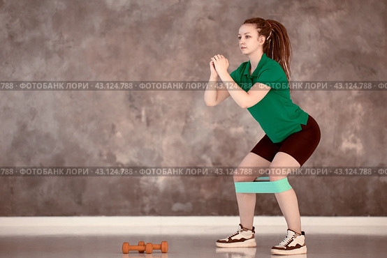 Sports elastic band for training on legs of serious caucasian woman in gym. Девушка выполняет упражнения со спортивной резинкой на коленях. Стоковое фото, фотограф Владимир Григорьев / Фотобанк Лори