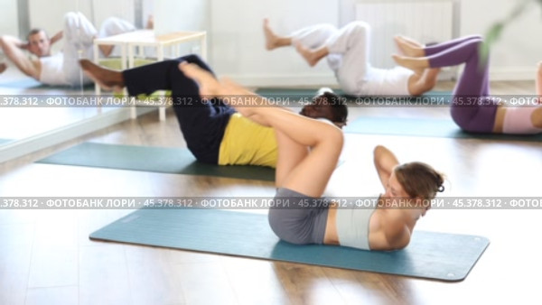 Sporty fit young female pilates instructor leading group classes for men and women of different ethnicities in studio, performing bicycle crunches to strengthen and stabilize abs and obliques. Стоковое видео, видеограф Яков Филимонов / Фотобанк Лори