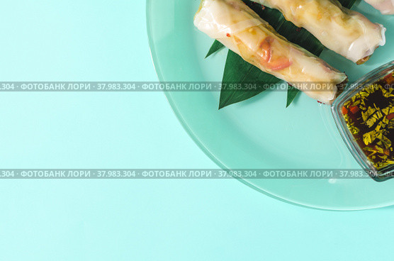 Спринг-роллы с морепродуктами и овощами, украшенные зелеными листьями, на светлом фоне. Стоковое фото, фотограф Лозовая Людмила / Фотобанк Лори