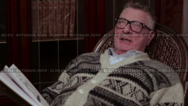 Старик в очках читает книгу вслух в кресле-качалке возле книжного шкафа. Стоковое видео, видеограф Video Kot / Фотобанк Лори