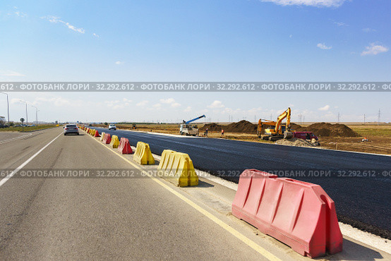 Строительство новой современной автомобильной дороги Таврида в Крыму. Свежий черный асфальт отделен желтыми и красными дорожными барьерами. Солнечный летний день. Стоковое фото, фотограф Наталья Гармашева / Фотобанк Лори
