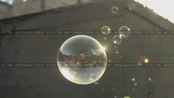 Sunlight streaming through large soap bubble, surrounded by smaller bubbles, creating iridescent display against blurred urban background, showcasing delicate fragility. Стоковое AI-видео, аниматор Юрий Поздников / Фотобанк Лори