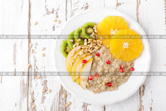 Sweet oatmeal porridge with pine nuts and fresh fruits - pear, orange, kiwi and pomegranate. Healthy dietary breakfast. Vegetarian dish. Стоковое фото, агентство Ingram Publishing / Фотобанк Лори