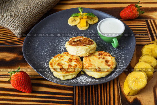 Syrniki or cheese pancakes with cream sauce and bananas on a plate on wooden table close up. Стоковое фото, фотограф Татьяна Терехина / Фотобанк Лори