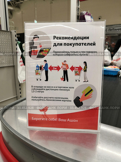 Табличка на кассе магазина Ашан с рекомендациями покупателям о соблюдении дистанции между людьми и мерах безопасности в связи с мероприятиями по пресечению распространения короновируса весной 2020 года. Редакционное фото, фотограф Александр Замараев / Фотобанк Лори
