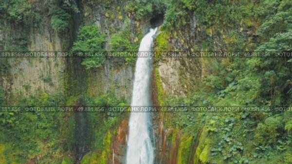 Tall waterfall pouring down mossy cliff into clear pool in Costa Rica. Стоковое видео, видеограф Igor Tichonow / Фотобанк Лори