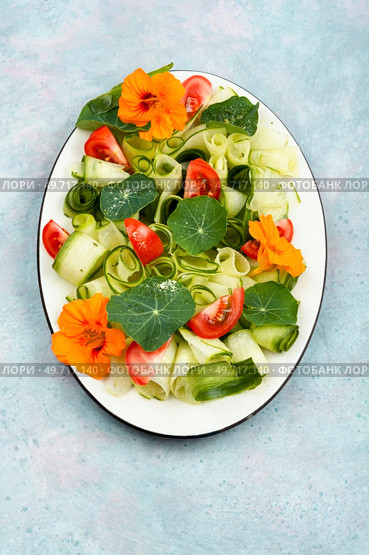 Tasty veggie salad with cucumber, tomato and nasturtium lettuce leaves and flowers. Flat lay.. Vegetable salad with nasturtium flowers. Стоковое фото, агентство Ingram Publishing / Фотобанк Лори