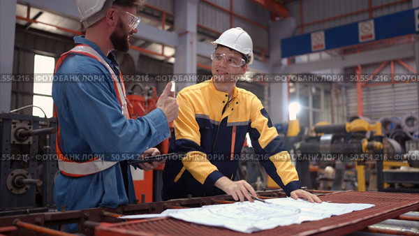 Team of engineers and architects working with blueprint at factory site. It is a massive new facility for making metal sheets as well as a transportation and distribution warehouse. Стоковое фото, агентство Ingram Publishing / Фотобанк Лори