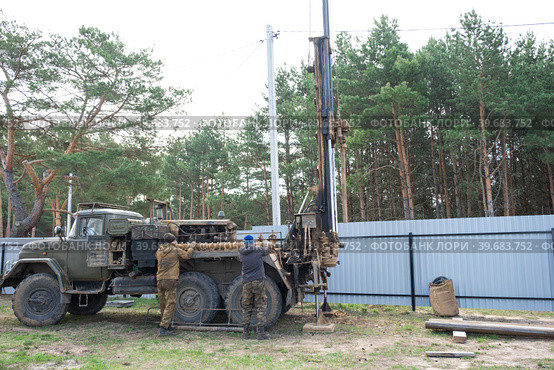 Team of workers with drilling rig on car are drilling artesian well for water in ground. Insertion of metal casing pipe into ground, installation of individual drinking supply, June 28, 2022, Russia, Стоковое фото, фотограф Ольга Симонова / Фотобанк Лори