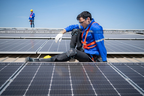 Technician repairing solar panels take off his hat and rest in the scorching sun on a factory roof covered with solar panels to receive solar energy. Стоковое фото, агентство Ingram Publishing / Фотобанк Лори