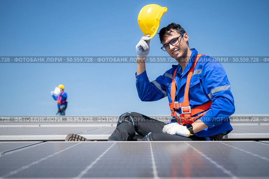 Technician repairing solar panels take off his hat and rest in the scorching sun on a factory roof covered with solar panels to receive solar energy. Стоковое фото, агентство Ingram Publishing / Фотобанк Лори