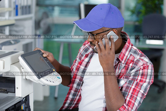 technician using a phone to fix a printer. Стоковое фото, агентство Ingram Publishing / Фотобанк Лори