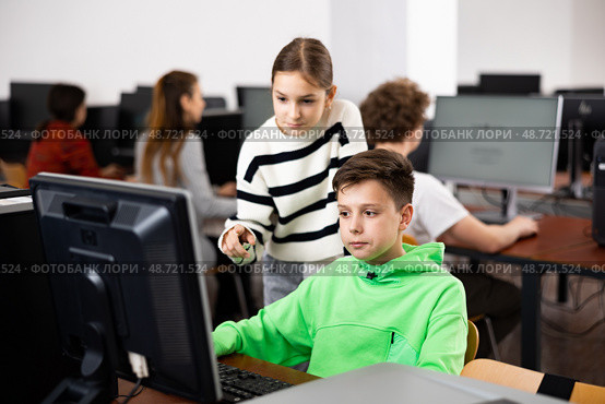 Teen schoolgirl talking to focused classmate in computer class. Стоковое фото, фотограф Яков Филимонов / Фотобанк Лори
