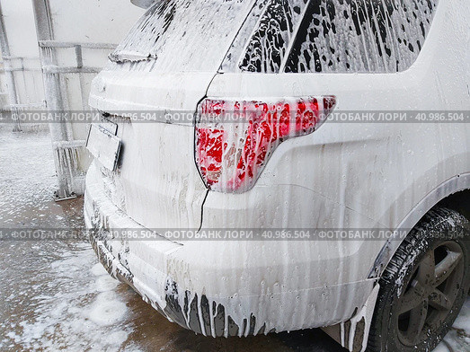 The back of the very dirty white SUV, doused with shampoo and foam, stands in the  box of outdoor self-service car wash and waits for washing. Очень грязный белый внедорожник, облитый шампунем и пеной, стоит в боксе уличной автомойки самообслуживания и ждет мойки. Стоковое фото, фотограф Дмитрий Березнев / Фотобанк Лори