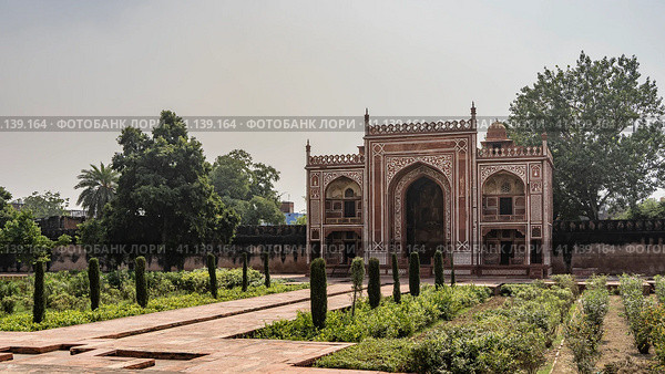 The building in the complex Tomb of Itimad-ud-Daulah is built of red sandstone and decorated with white ornaments. Visible arches, dome. Green vegetation grows on the sides of the paved path. India. (2022 год). Стоковое фото, фотограф Вера Ивановна Кубарева / Фотобанк Лори