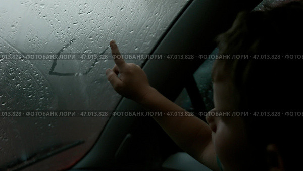 The child draws pictures with his finger on a wet misted window on a cloudy day. Стоковое фото, фотограф David Kashakhi / Фотобанк Лори