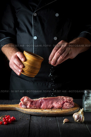 The cook prepares raw veal meat. Before baking, the chef adds salt to the beef. National dish is being prepared in the restaurant kitchen.. The cook prepares raw veal meat. Before baking, the chef adds salt to the beef. National dish is being prepared in the restaurant kitchen. Стоковое фото, агентство Ingram Publishing / Фотобанк Лори