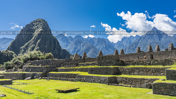The famous archaeological complex of Machu Picchu. Stone terraces, a field with green grass, ruins of buildings against the background of mountains and blue sky. Majestic Wayna Pikchu. Стоковое фото, фотограф Вера Ивановна Кубарева / Фотобанк Лори