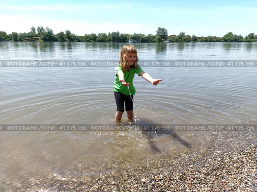 The girl stands knee-deep in the water and stretches her arms forward. A child at the pond. A girl with long white hair smiles and plays with drops and splashes. Serbia, Sava River, Sremska Mitrovica. Стоковое фото, фотограф Юлия Петровская / Фотобанк Лори