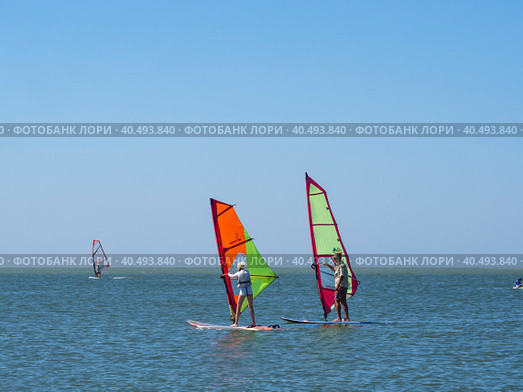 The instructor teaches the girl to control windsurfing. A calm sea where you can do water sports on a sailing board. Great time at sea with windsurfing and surfing. Russia, Yeysk, August 5, 2020. Редакционное фото, фотограф Александр Кротков / Фотобанк Лори