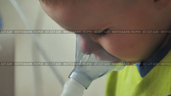 The kid is breathing with an inhaler and watching a cartoon. Стоковое видео, видеограф Mikhail Davidovich / Фотобанк Лори