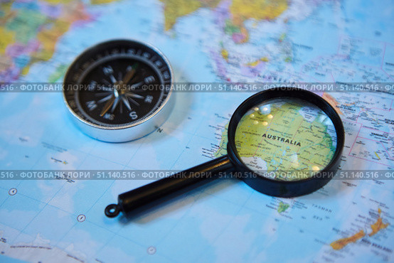 The magnifying glass is located on the world map and magnifies the country of Australia. There's a compass next to it. Concept of travel in the selected country. Стоковое фото, фотограф Наталия Кирсанова / Фотобанк Лори