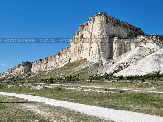The majestic White Rock (Ak-Kaya), located in Crimea, near the town of Belogorsk. This is one of the most recognizable and picturesque natural wonders of the peninsula. Snow-white limestone cliffs rise above the steppe valley, creating a contrast between the bright blue sky, dry grasses and light rocks. The rock looks monumental, as if it keeps ancient secrets - it really has archaeological and historical significance.White Rock (Ak-Kaya) is a limestone cliff about 100 meters high, formed in the Cretaceous period. This is a place of archaeological finds, legends, filming and inspiration for artists and poets. Стоковое фото, фотограф Анна Кривицкая / Фотобанк Лори