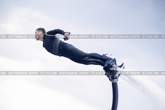 The man in a wetsuit seems to be flying like a superhero in the air against the background of the sky above the water, he is an athlete and a pilot of a hydroflight or a flyboard. Стоковое фото, фотограф Владимир Разгуляев / Фотобанк Лори