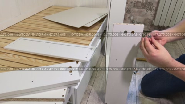 The man is assembling pull-out shelves for the sofa bed from wooden panels. He installs furniture cam locks. Стоковое видео, видеограф Vadzim Yakubovich / Фотобанк Лори