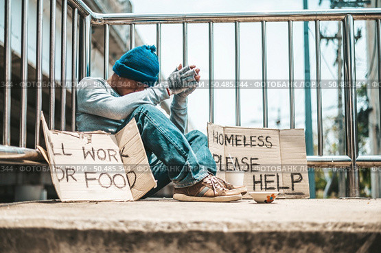 The man sitting begging on an overpass with messages homeless people please help and work well with food. Стоковое фото, агентство Ingram Publishing / Фотобанк Лори